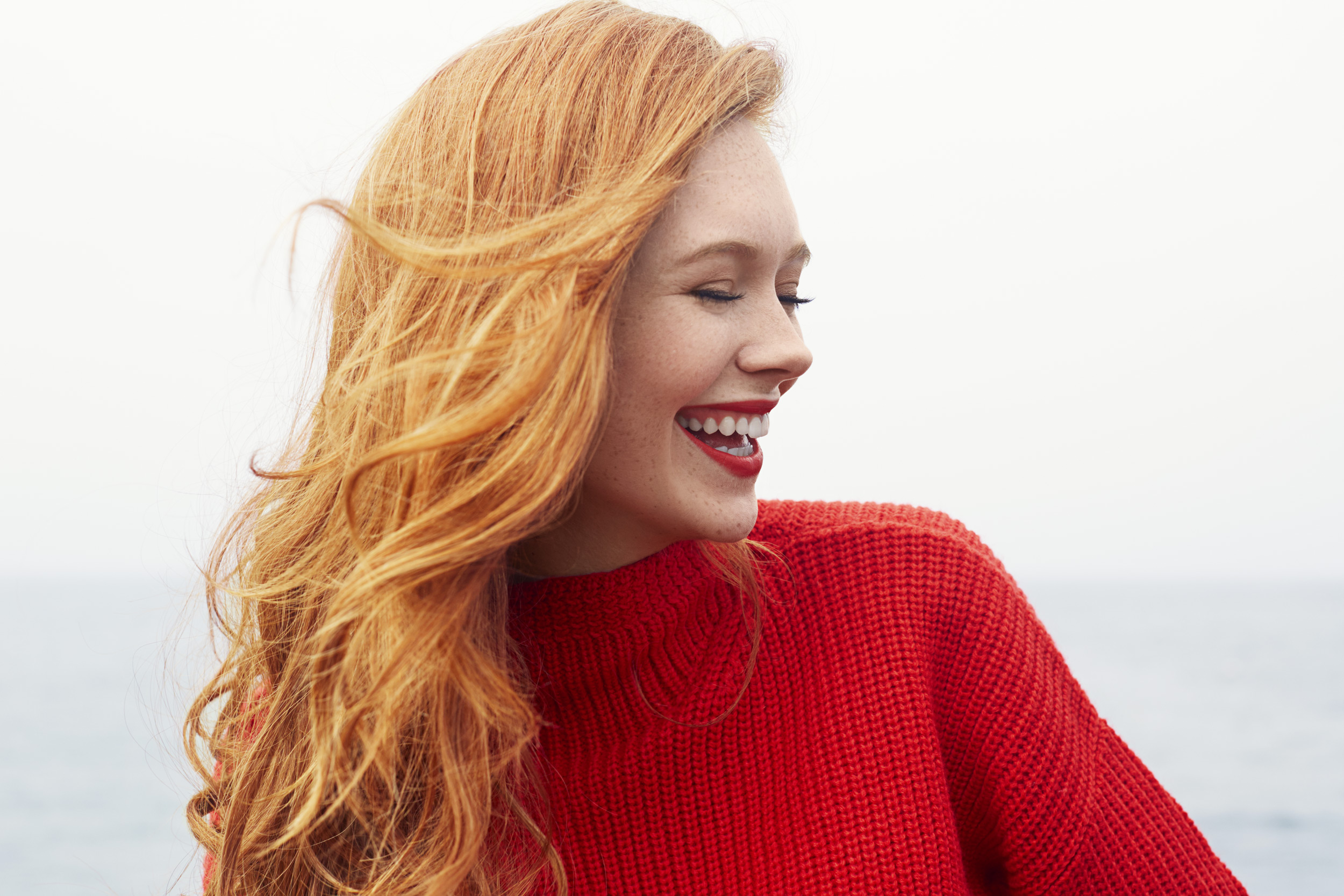 Millennial girl with red hair wearing a red sweater at the beach